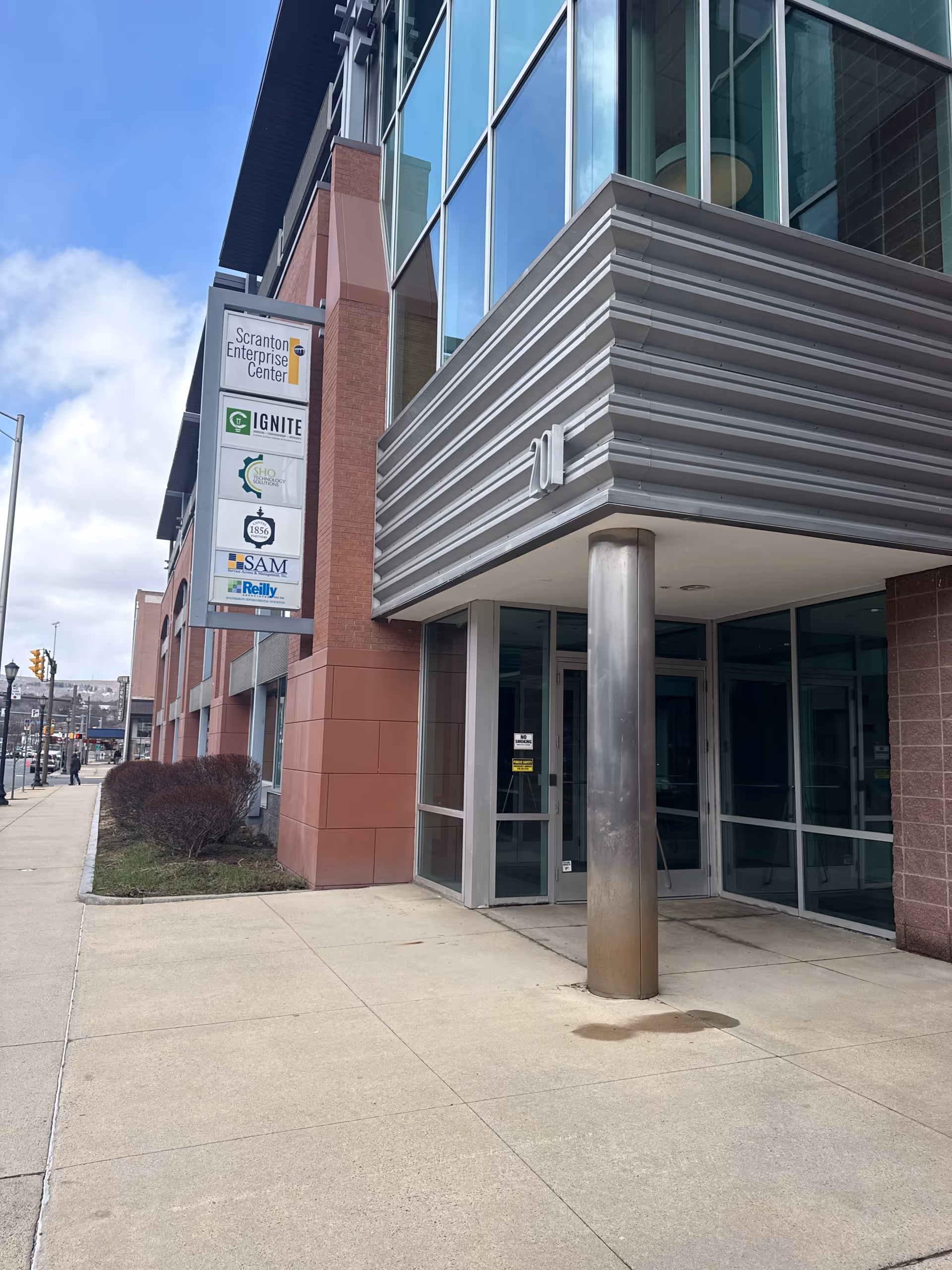 Modern glass-front building exterior with a covered entrance and sidewalk.