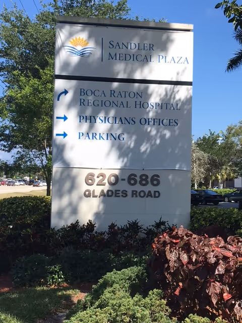 Tall outdoor sign for Sandler Medical Plaza and Boca Raton Regional Hospital with directions.