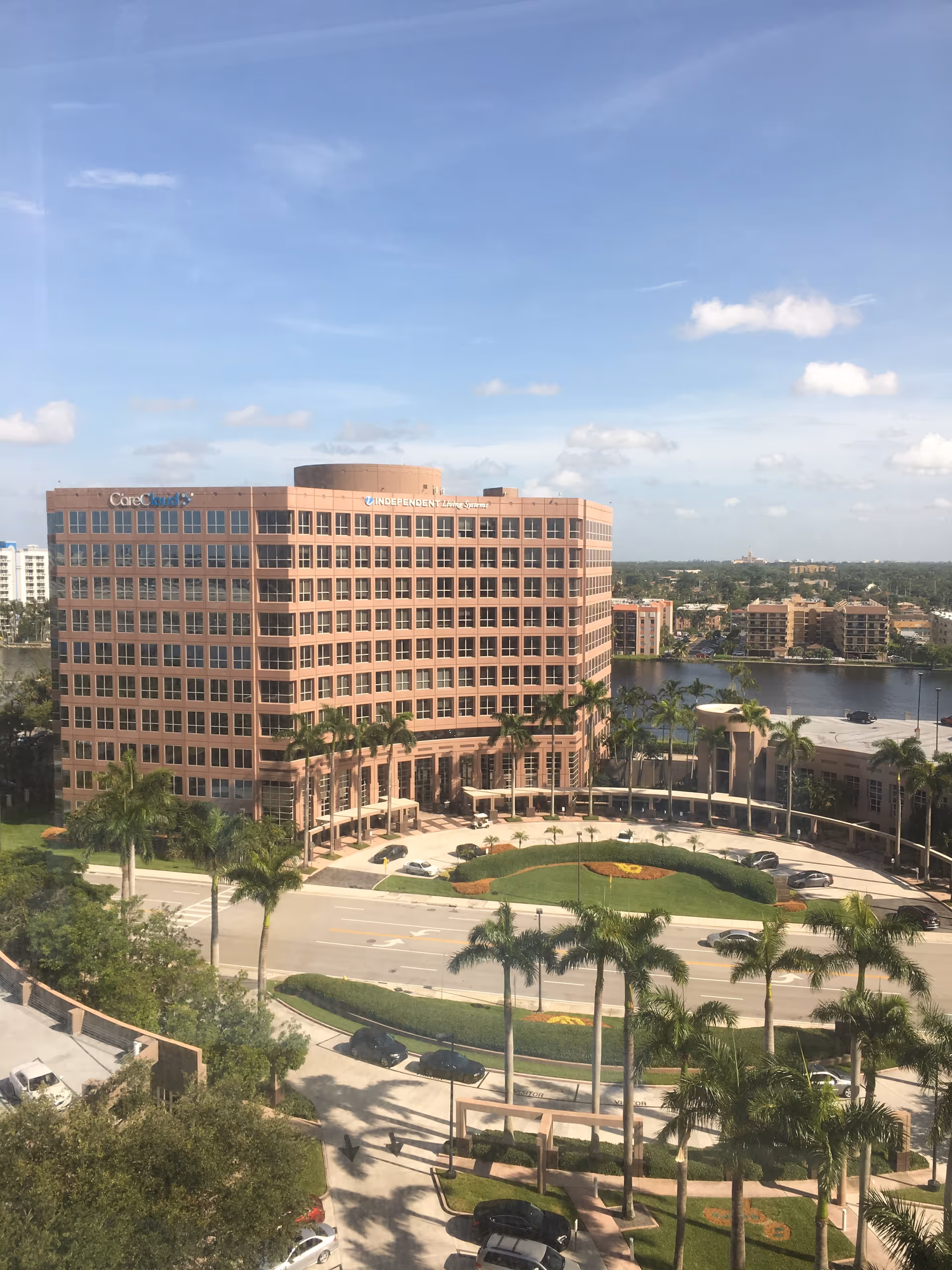 Tall pink-brick senior living building with palm trees and circular driveway.