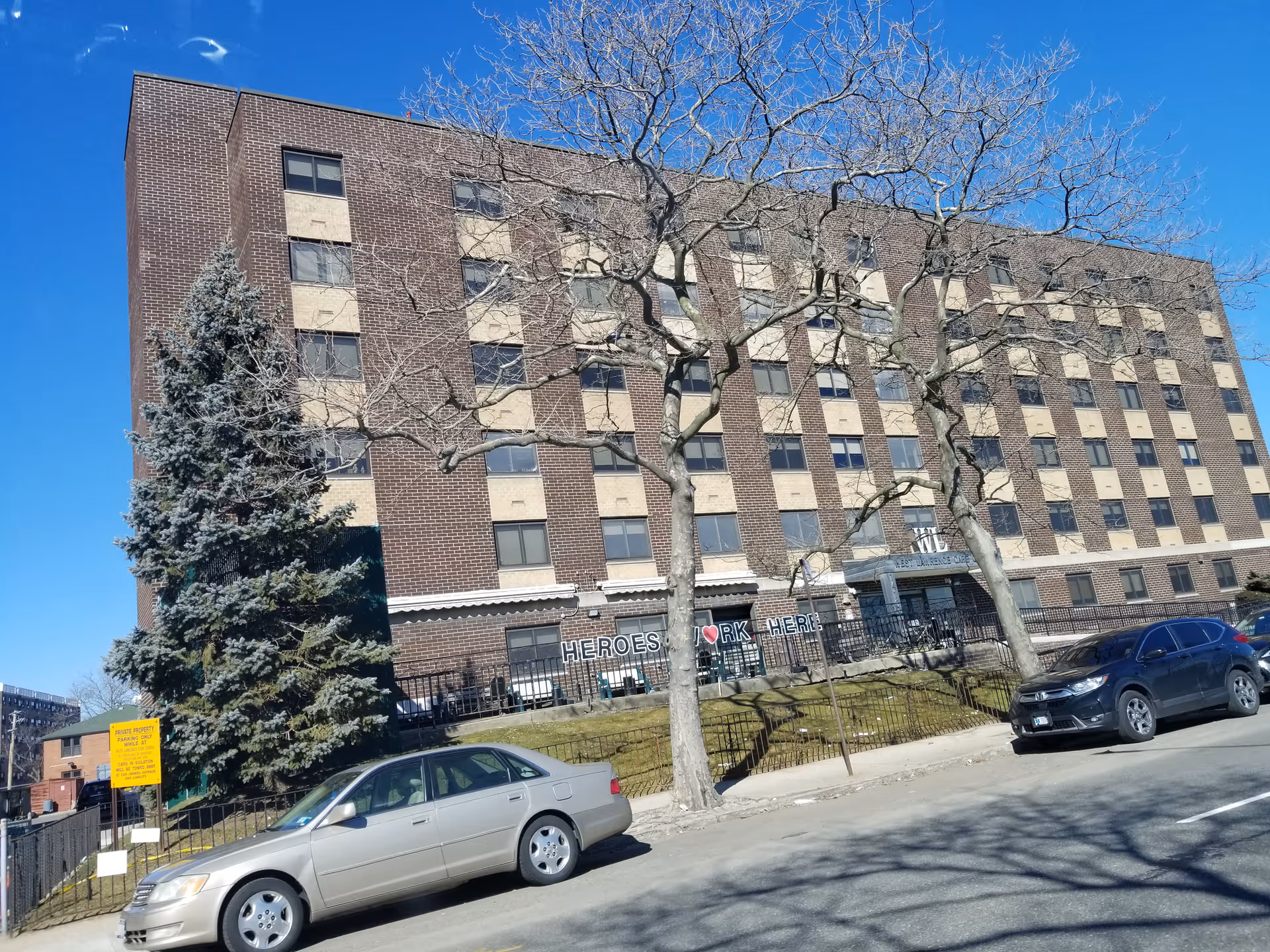 Brick multi-story senior care center front view with leafless trees and parked cars