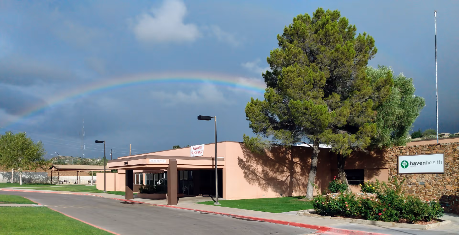 Haven Health Globe exterior building front with rainbow in cloudy sky.