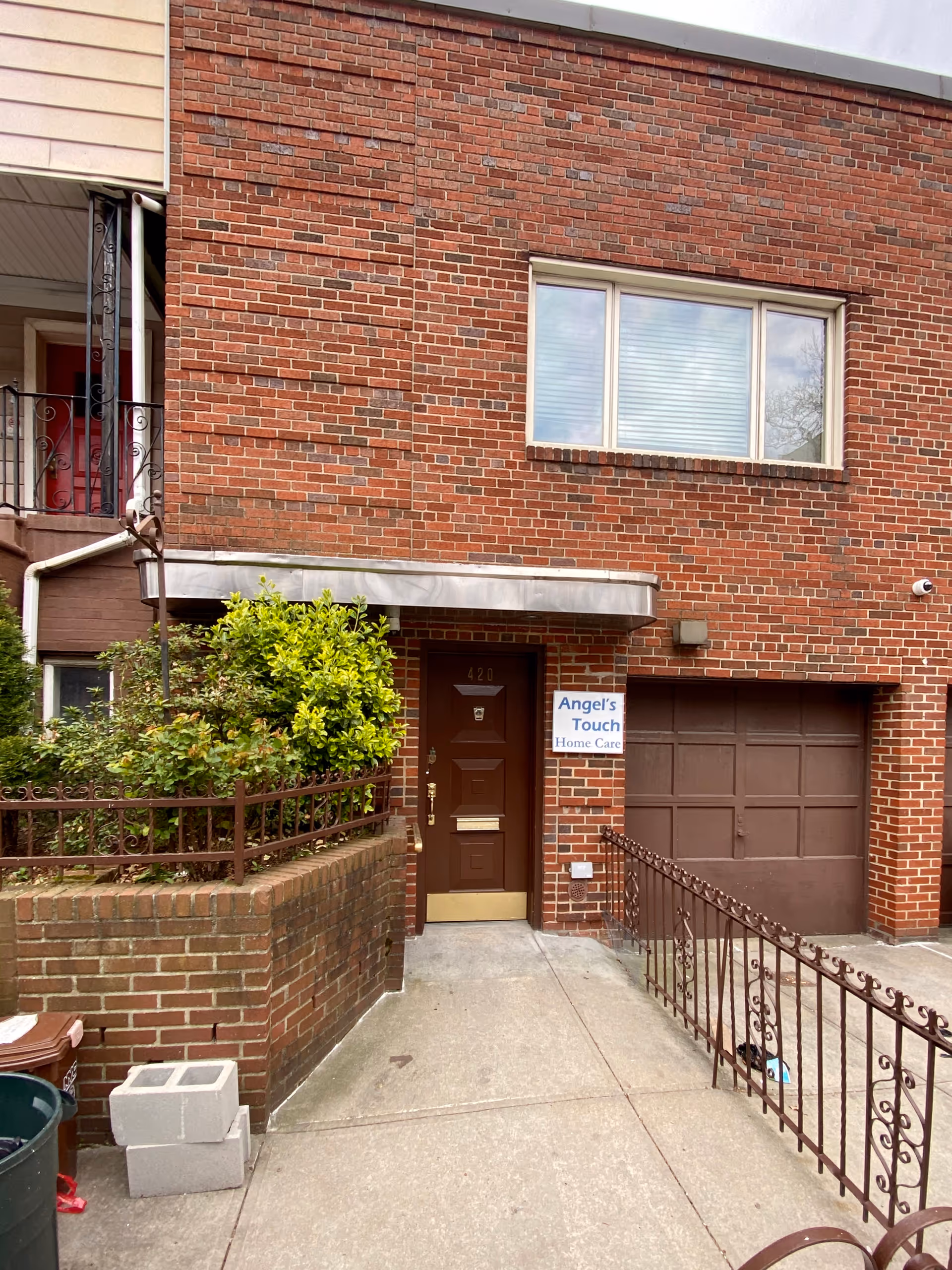 Brick building front with entrance door, window, railing, plants, and Angel's Touch Home Care sign.
