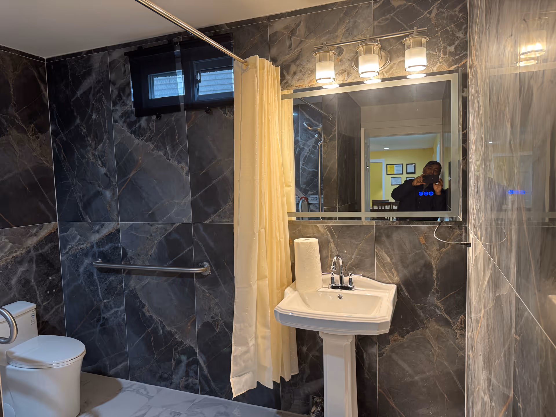 Bathroom with dark marble tiles, pedestal sink, toilet, shower curtain, and mirror.
