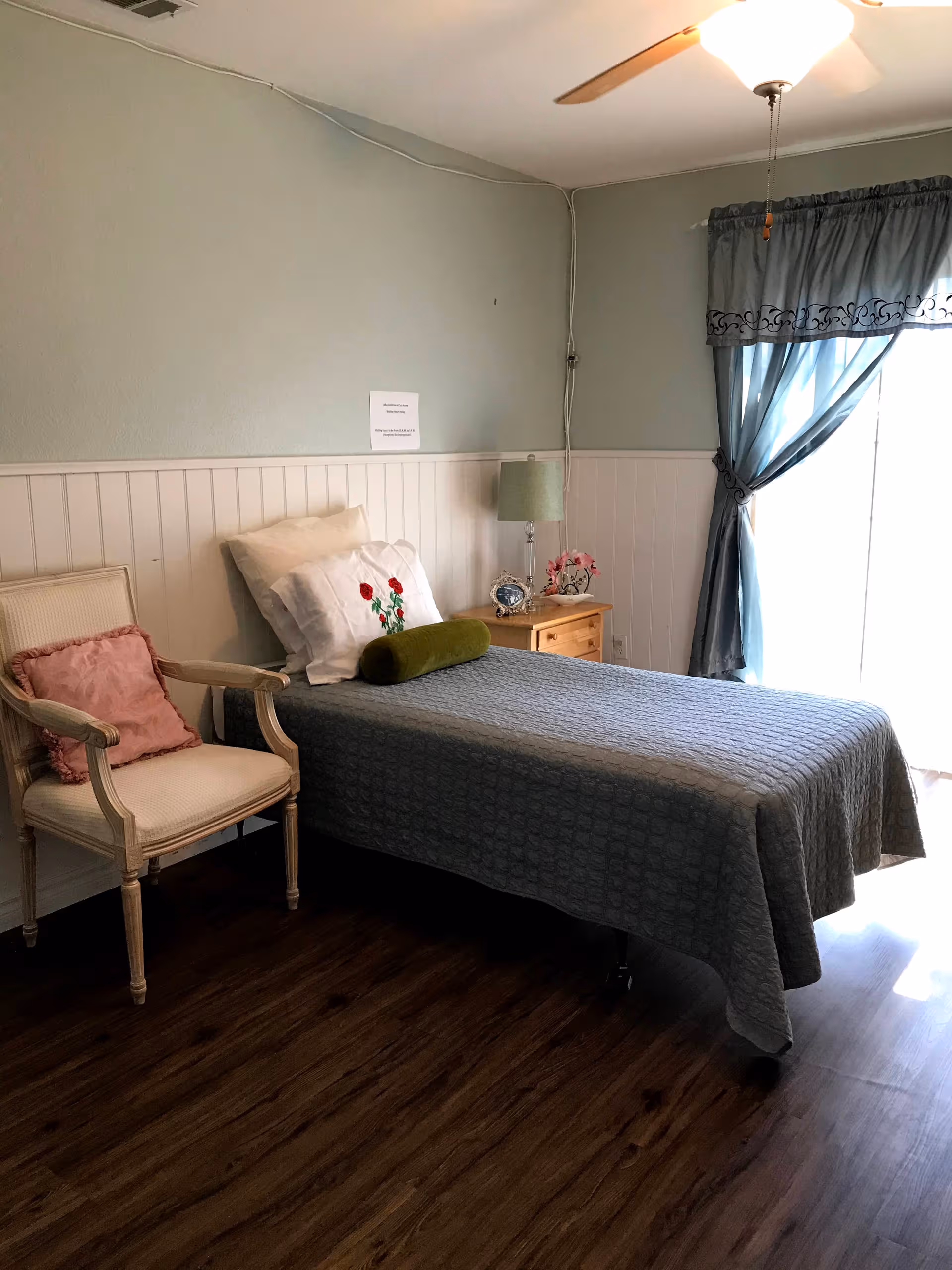 Cozy bedroom with a bed, pillows, chair, nightstand, and blue curtains.