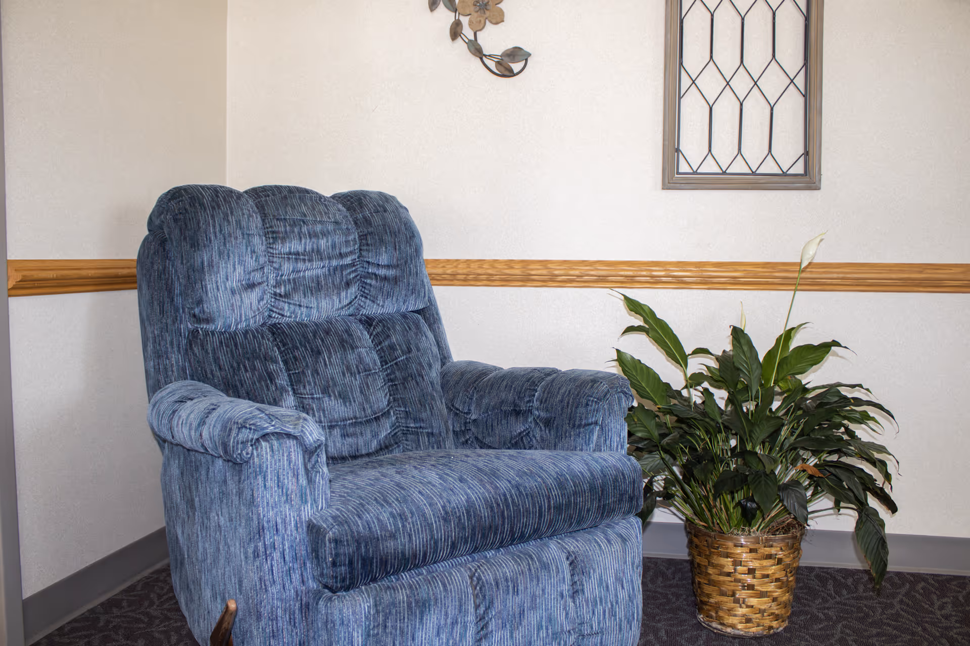 Blue upholstered armchair beside a potted plant in a beige-walled living room corner.