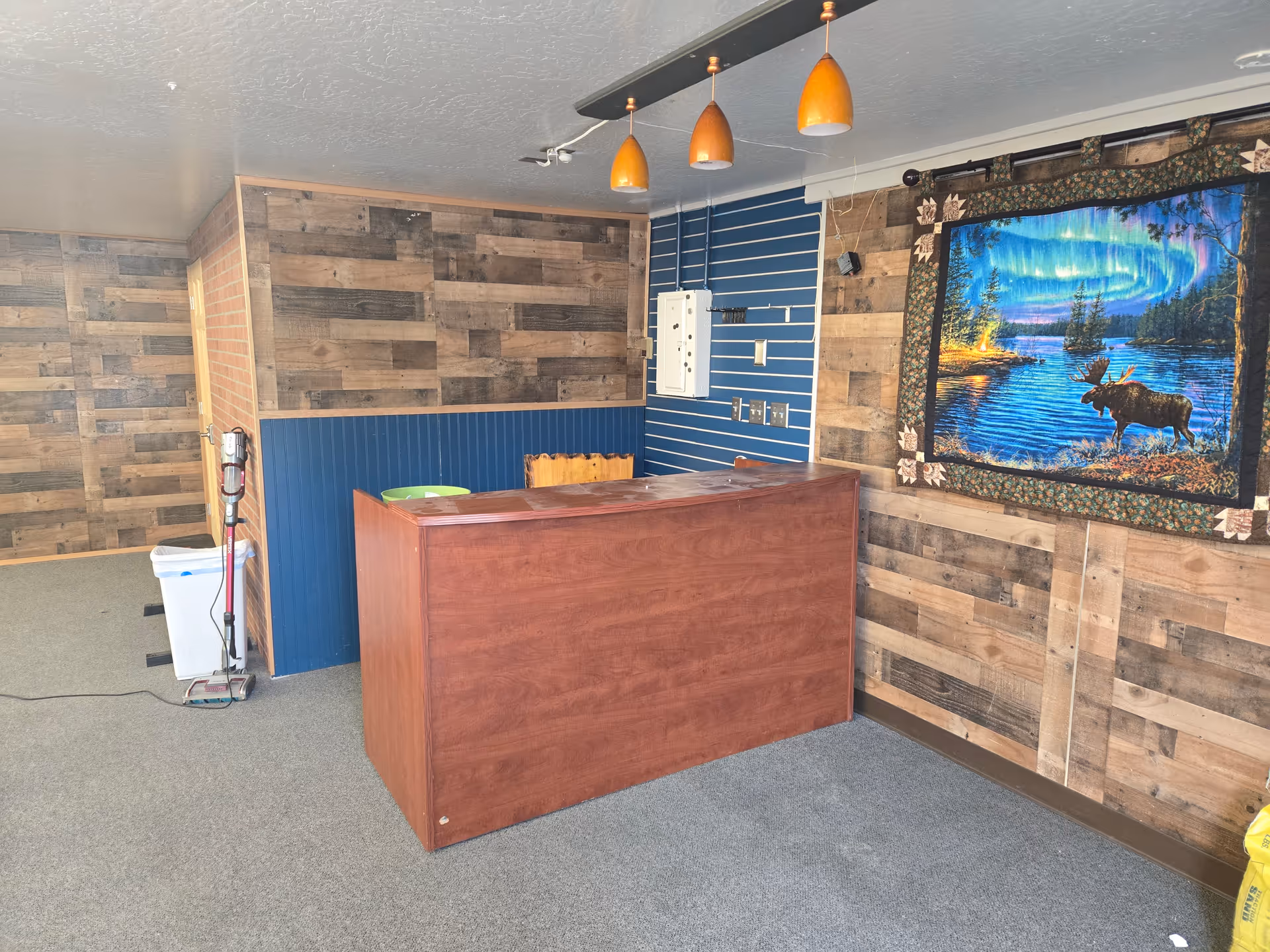 Wood-paneled interior with a reception desk, blue wall, moose artwork, and orange pendant lights.