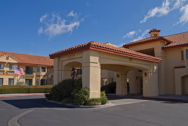 Exterior view of Whispering Winds of Apple Valley with arched entrance and flag