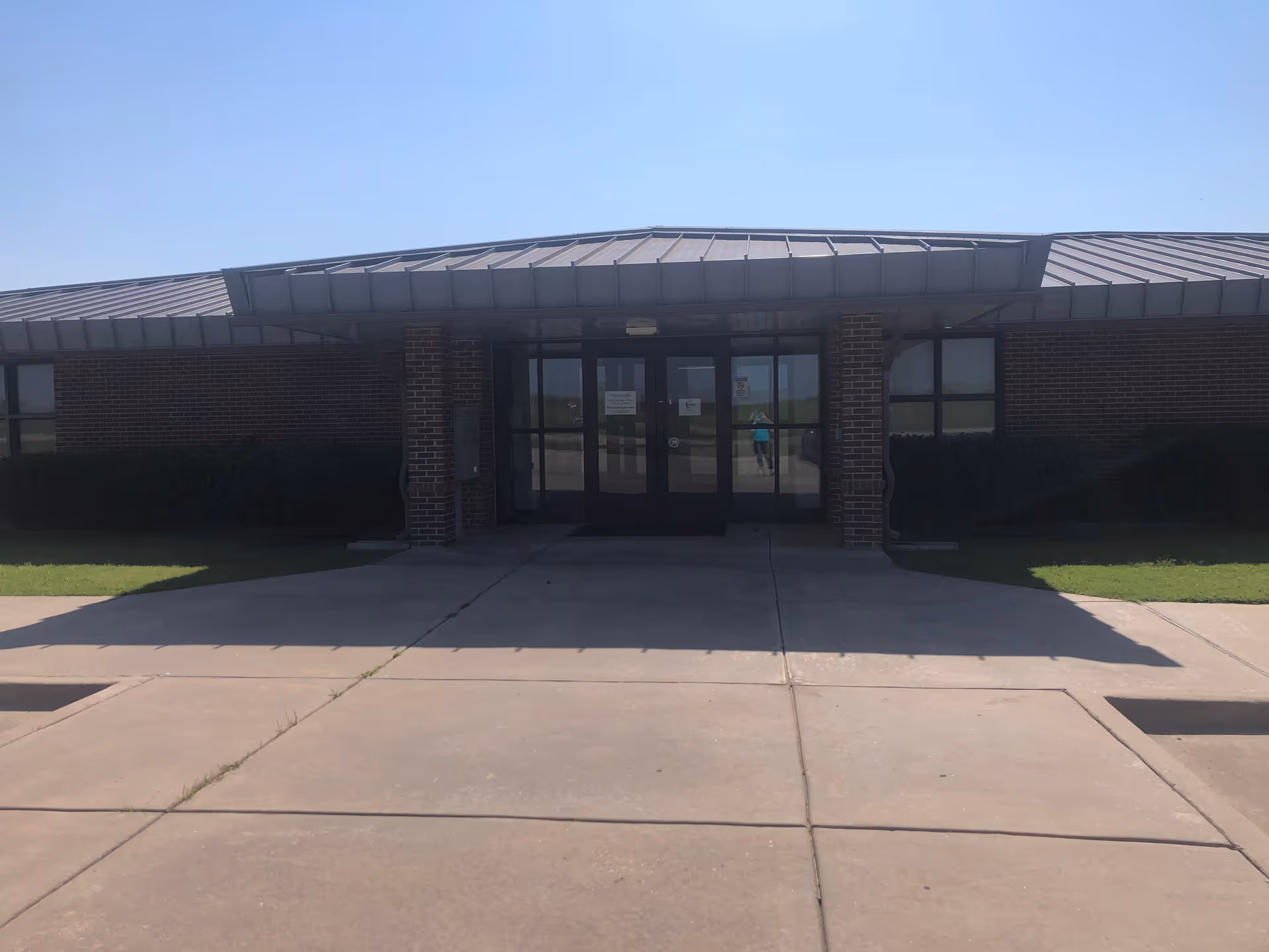 Brick building entrance with glass doors under a metal canopy and a sidewalk.