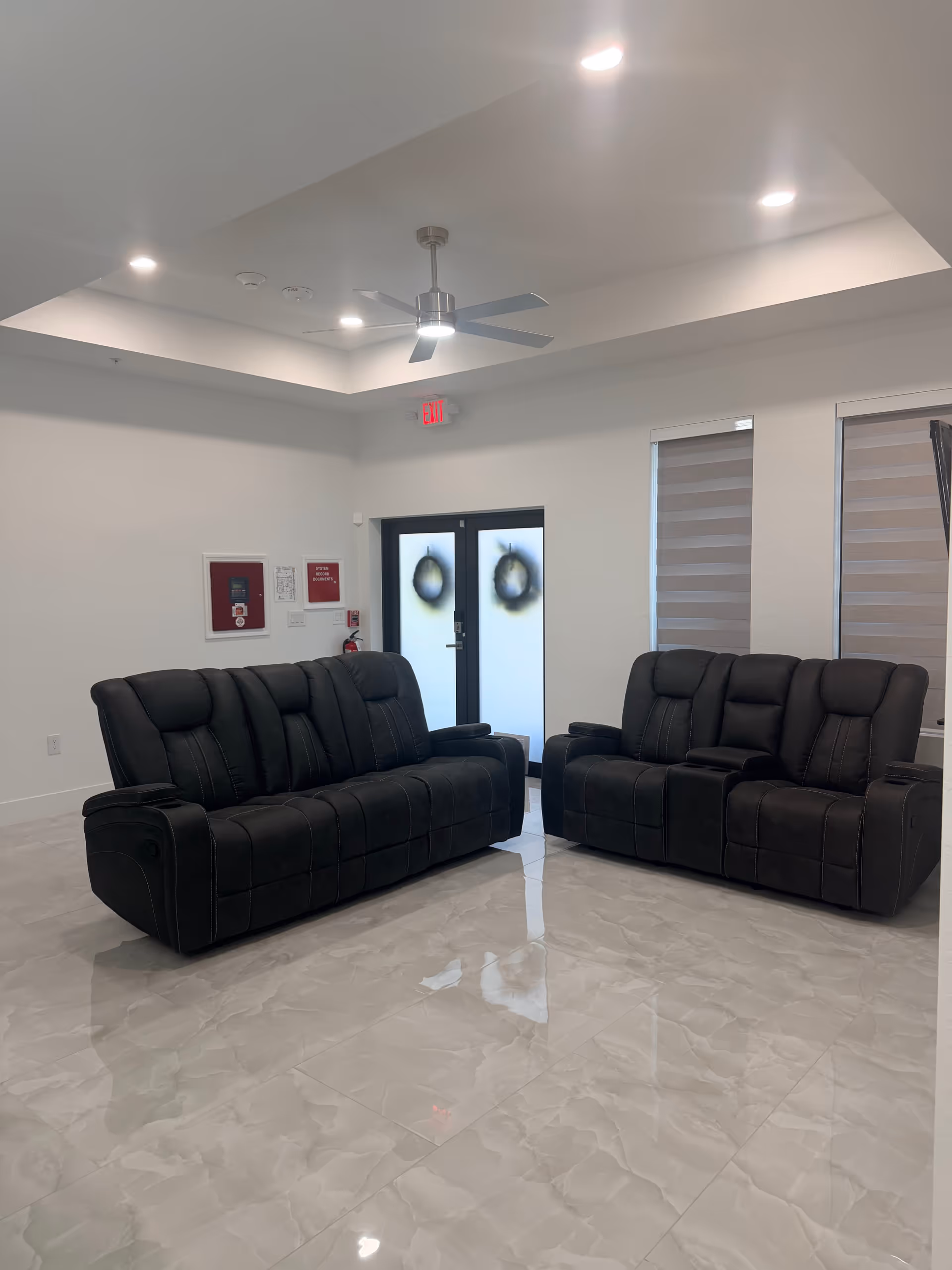 Two black leather recliner sofas sit in a bright, modern senior living lounge.