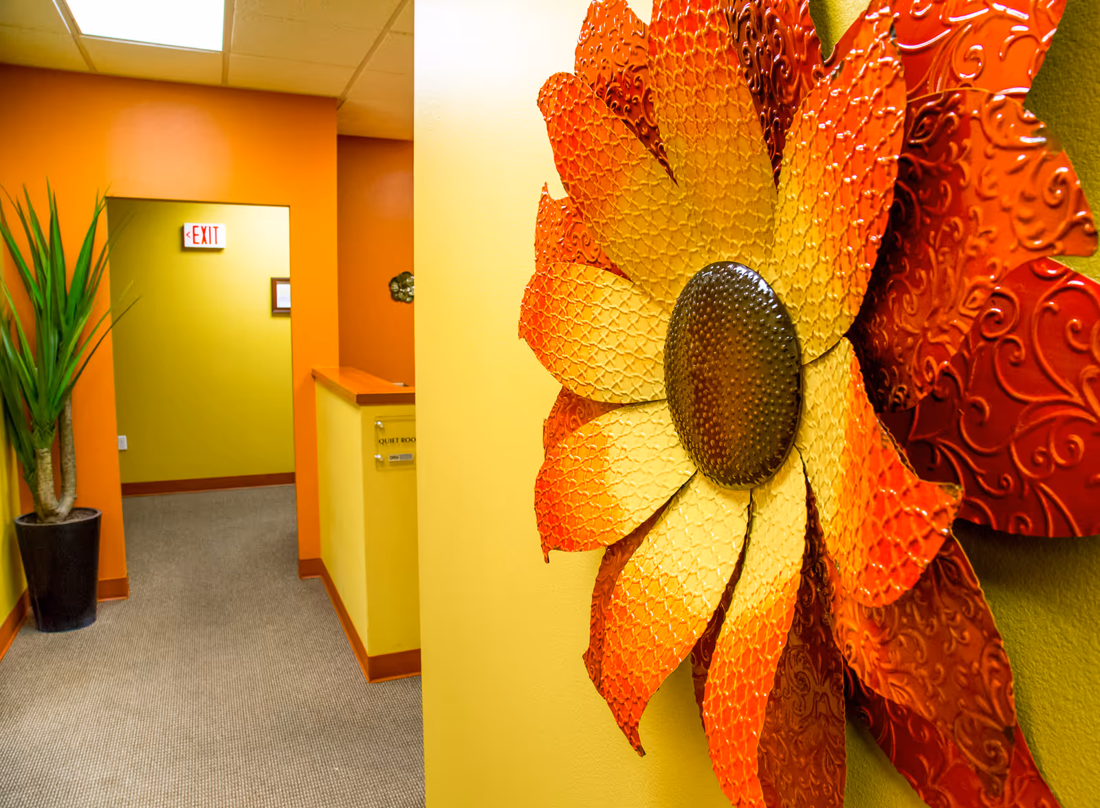 Bright hallway with orange and yellow walls, a large decorative flower sculpture on the right.
