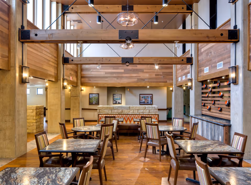 Interior dining area with wooden beams, tables, chairs, and a stone counter.