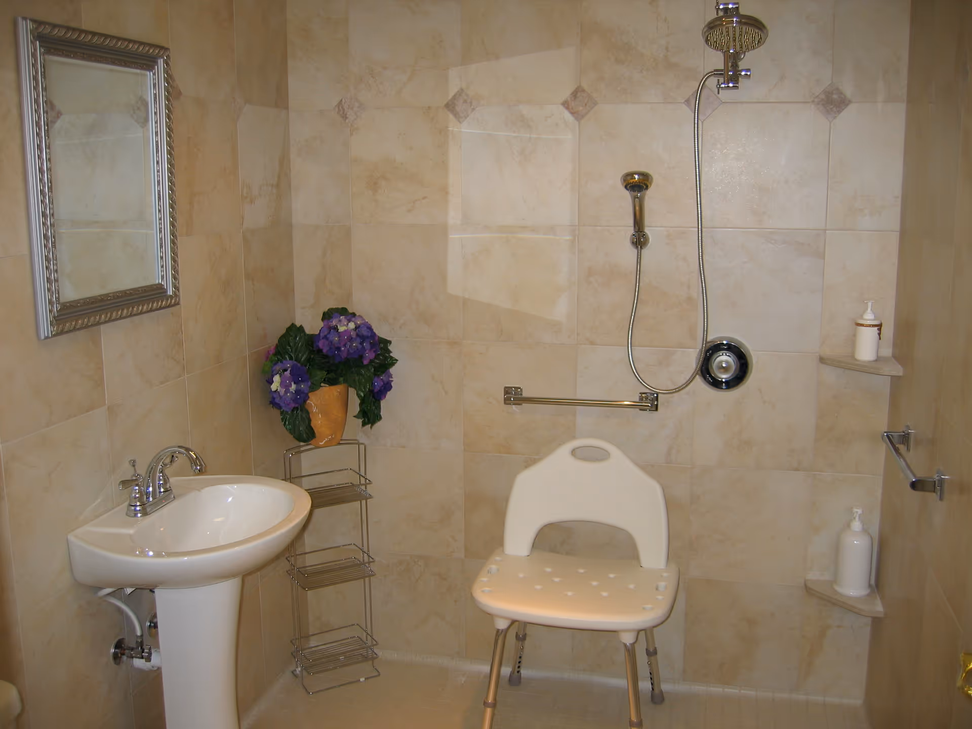 Tiled bathroom with sink, mirror, shower, and a white plastic chair.