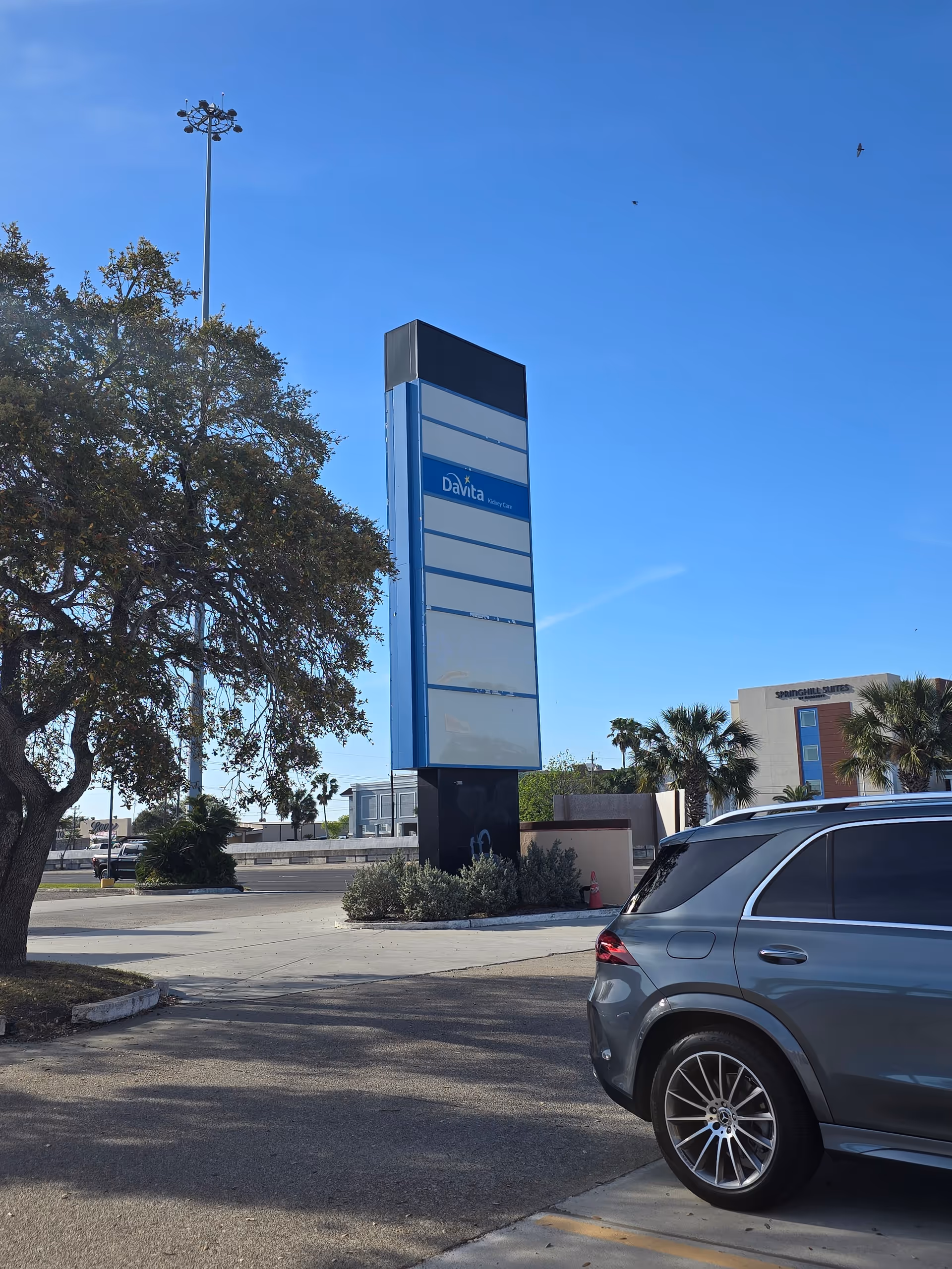 Tall blue and white vertical sign in a parking lot beside a silver SUV.