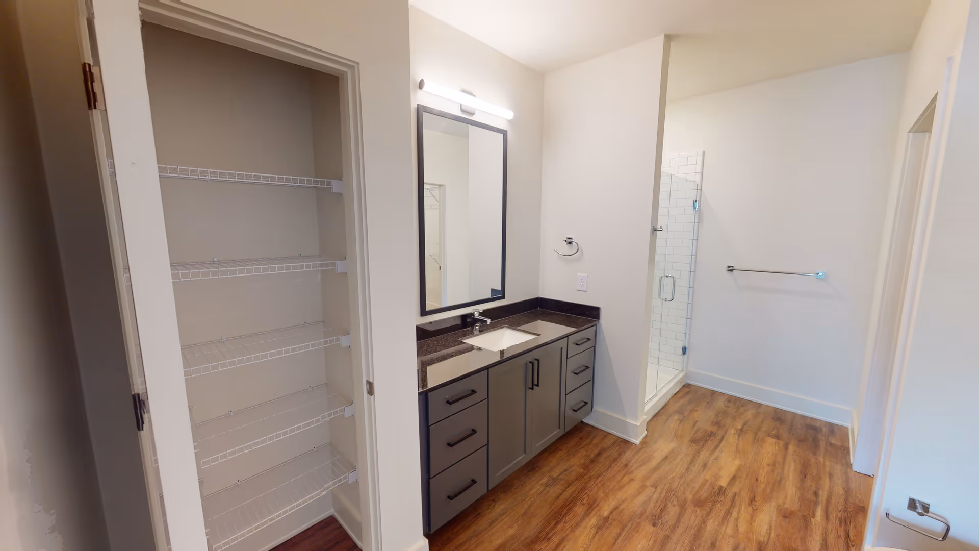 Modern bathroom with a vanity, sink, mirror, open closet shelves, and a glass shower.