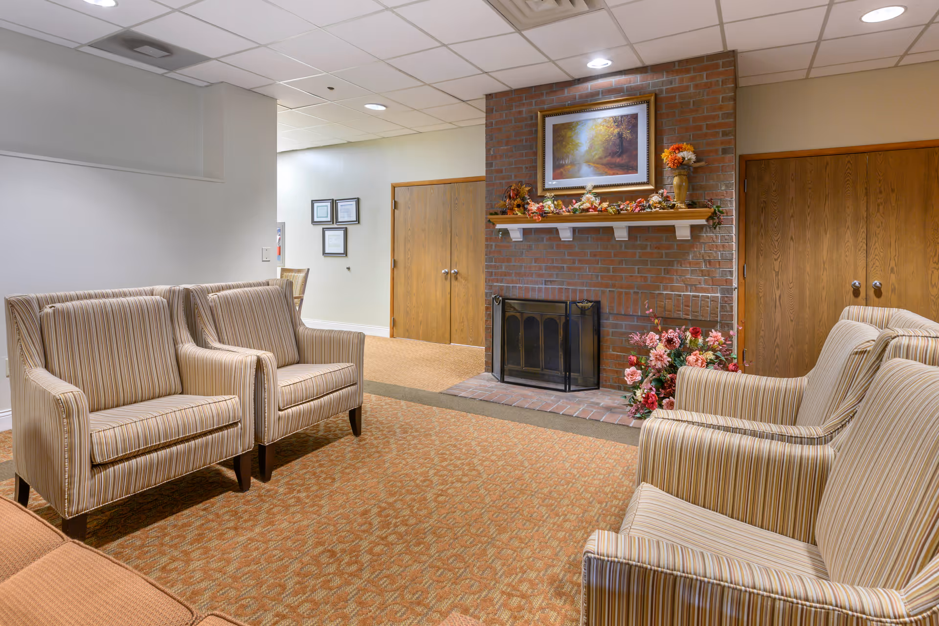 Cozy senior living lounge with striped armchairs, a brick fireplace, and floral accents.