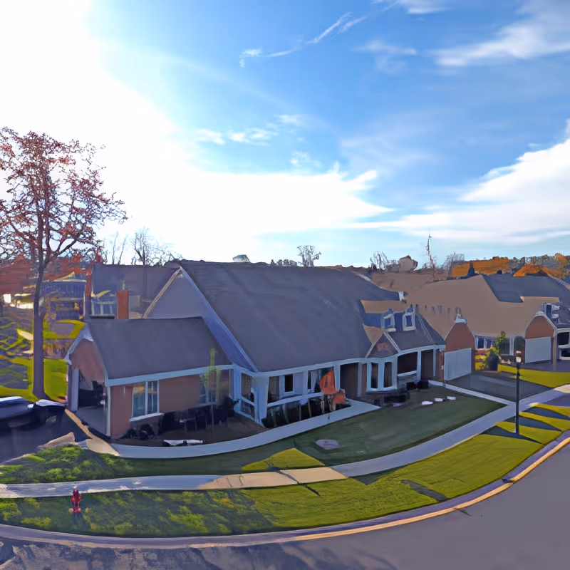 Front exterior of a single-story care facility with a steep roof, landscaped lawn, and curved walkway under a blue sky.