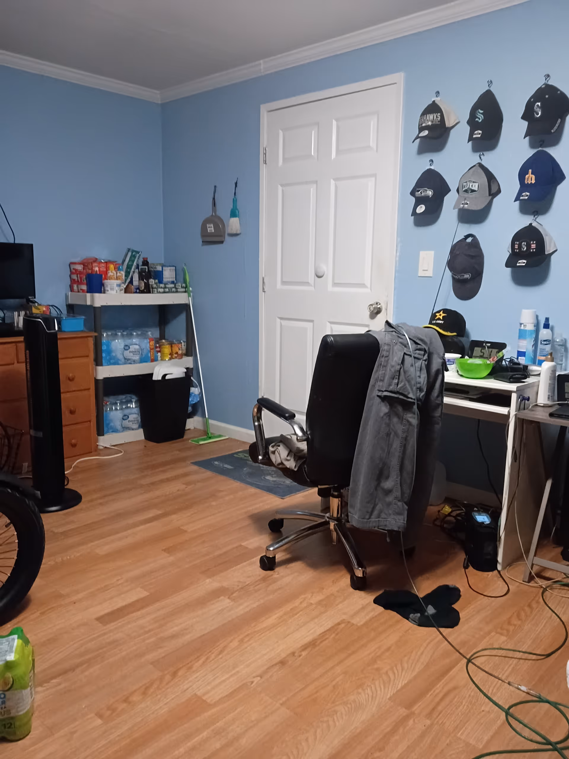 Blue-walled interior room with desk, chair, jacket draped, and hats hung on wall.