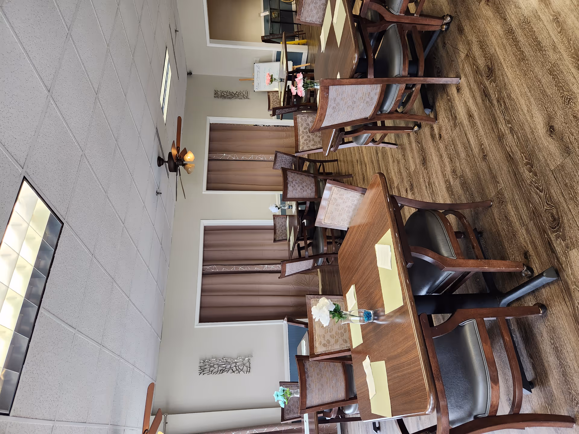 Empty senior living dining room with wooden tables, chairs, and floral centerpieces.
