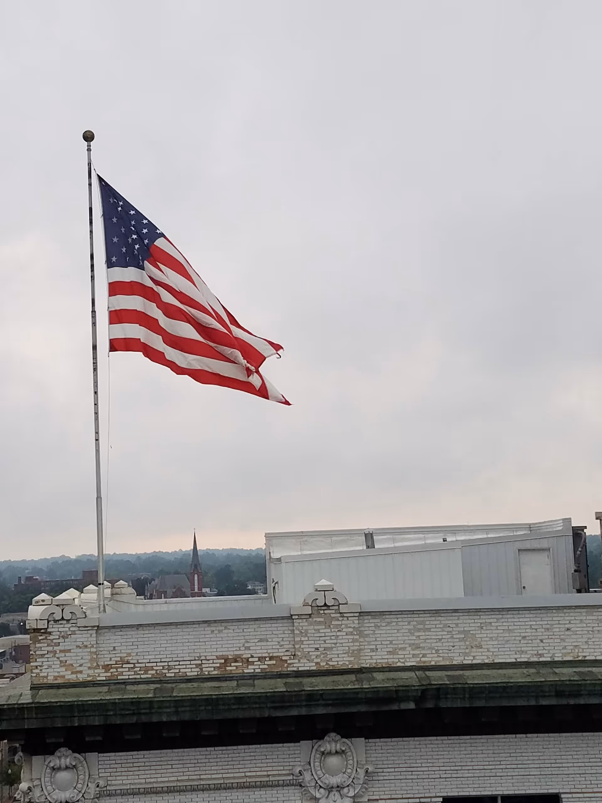 American flag waves above a brick building rooftop against a cloudy sky.