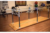 Rehabilitation gym area with parallel bars and exercise equipment on polished wood floor.