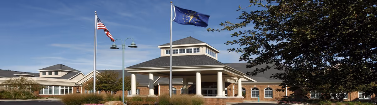Facade of Hartsfield Village senior living facility with flagpoles, a porte-cochère, and trees.