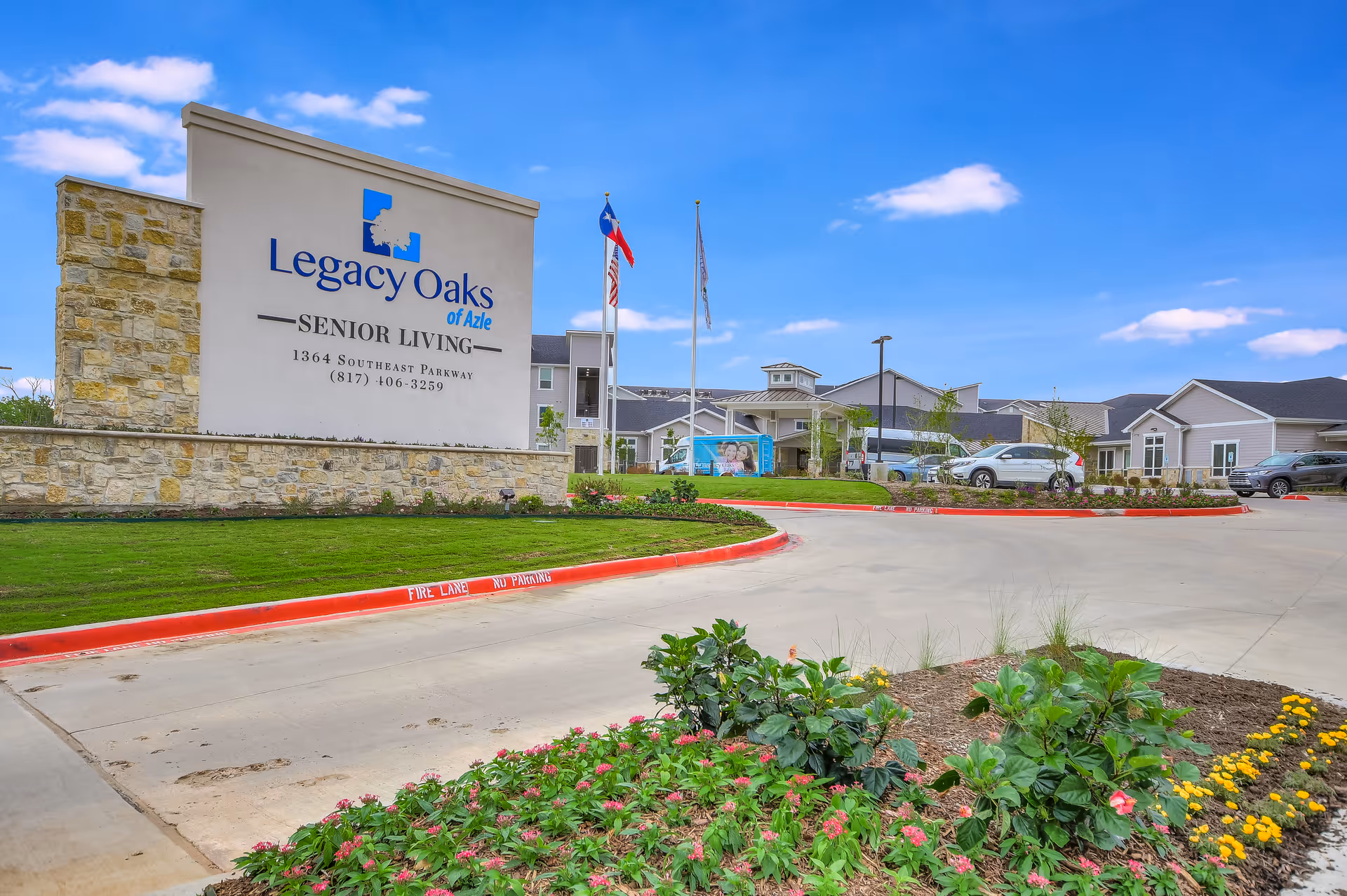 Front exterior view of Legacy Oaks of Azle Senior Living with sign, lawn, and parked cars.