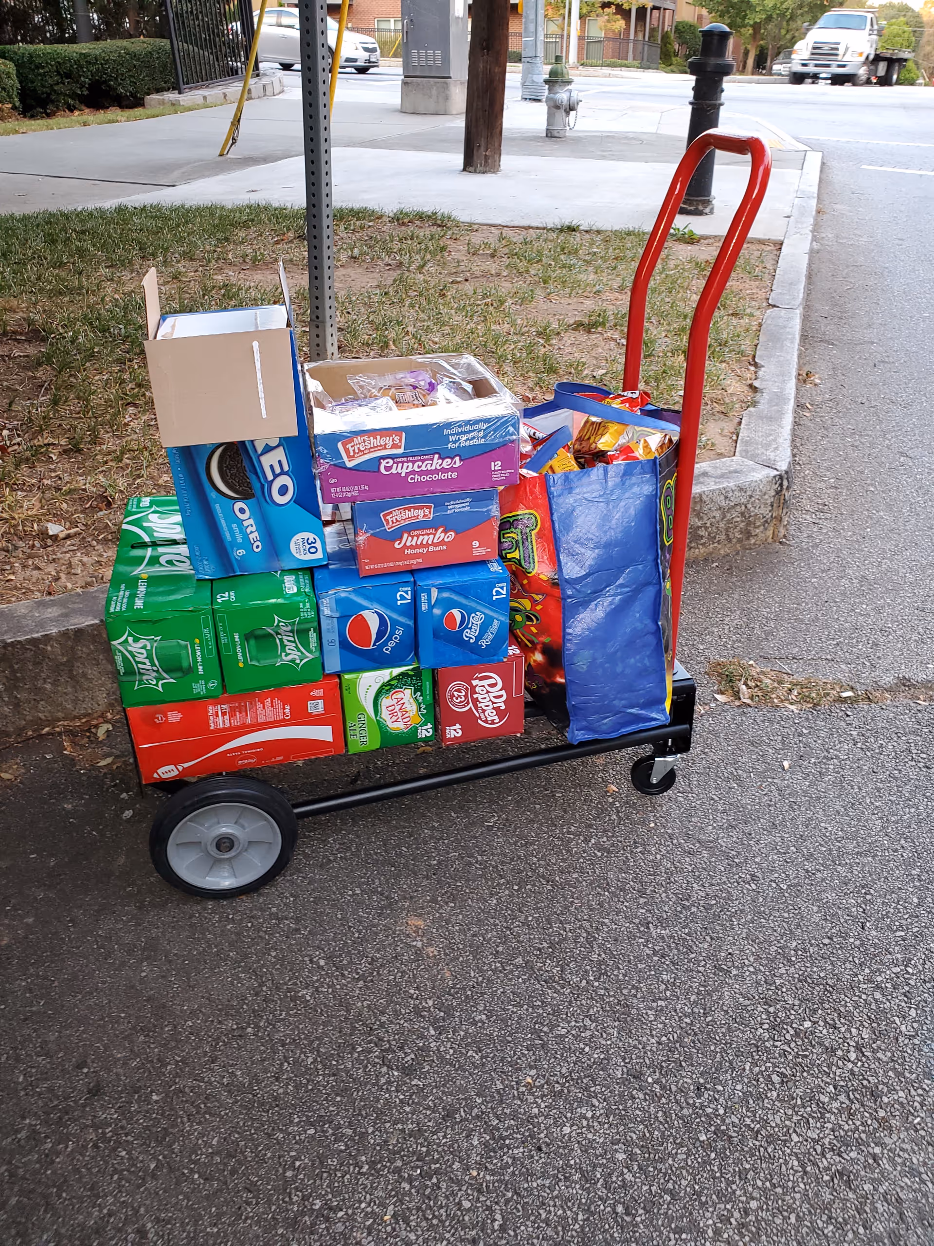 Grocery cart loaded with snack boxes sits on a sidewalk near a street.