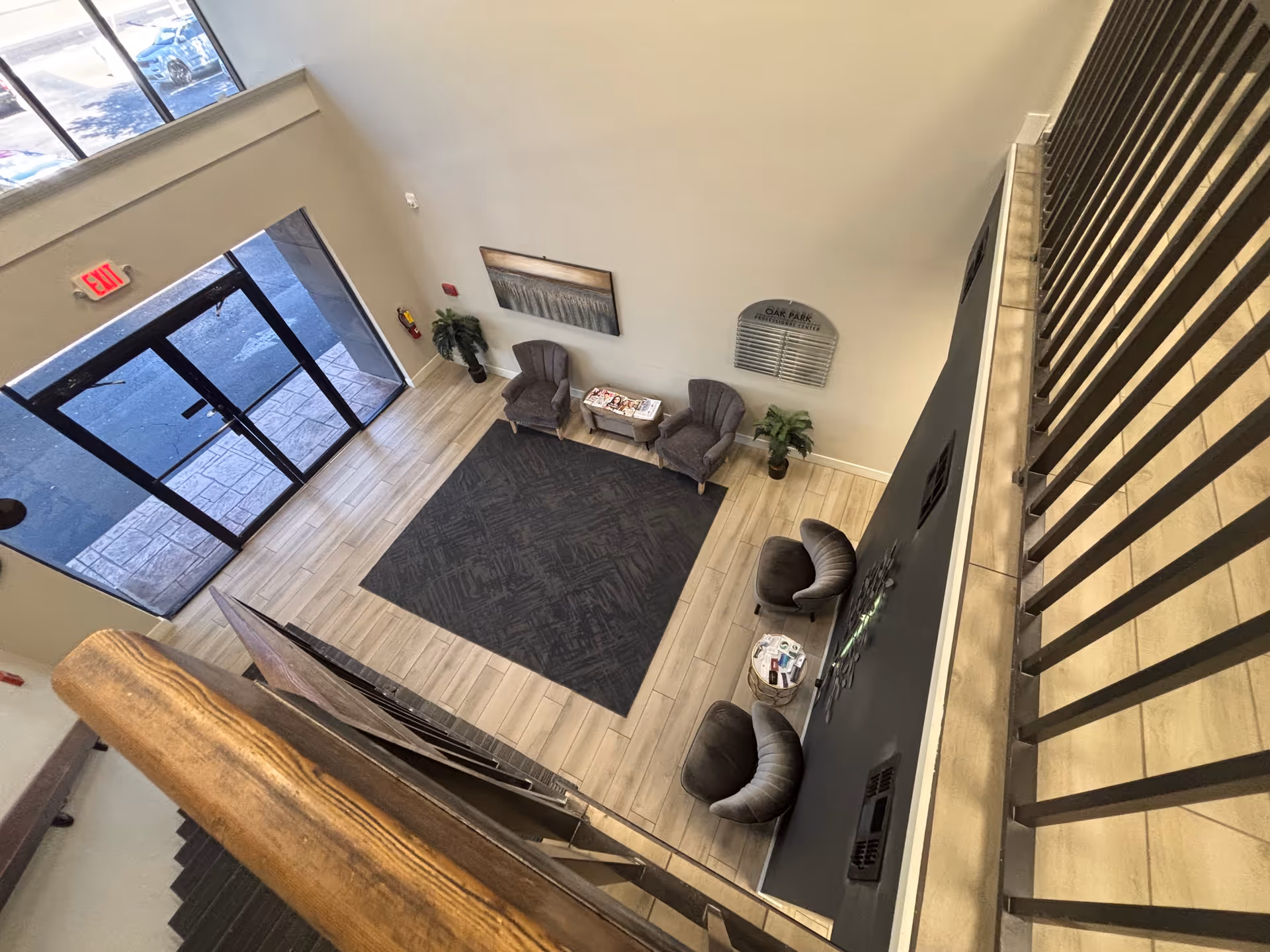 View from the upper stairwell of a lobby with seating, magazines, plants, and glass entry doors.