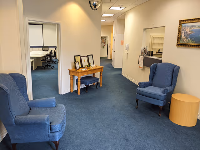Hallway lounge area in a senior living facility with blue upholstered chairs and a small table.