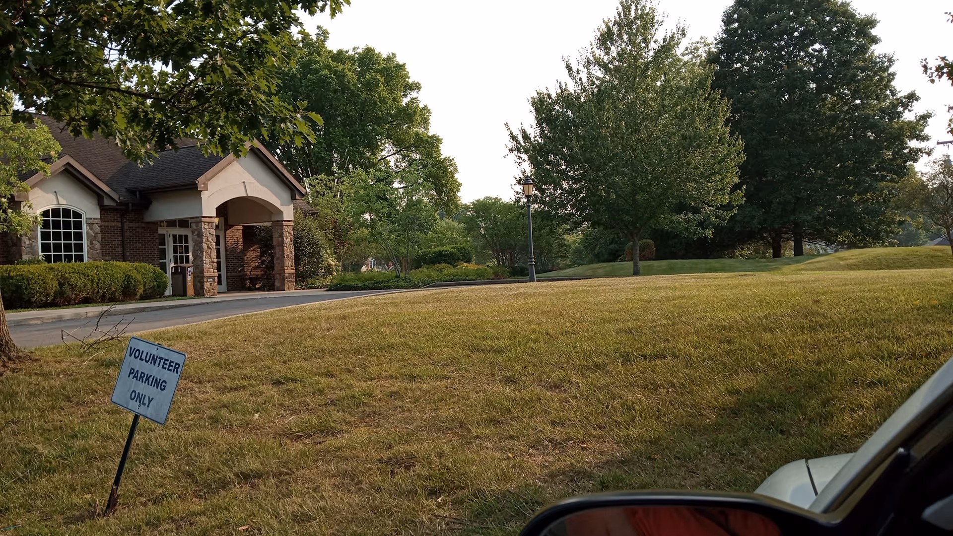 Front exterior of a senior care facility with a parking area, sign, and trees.