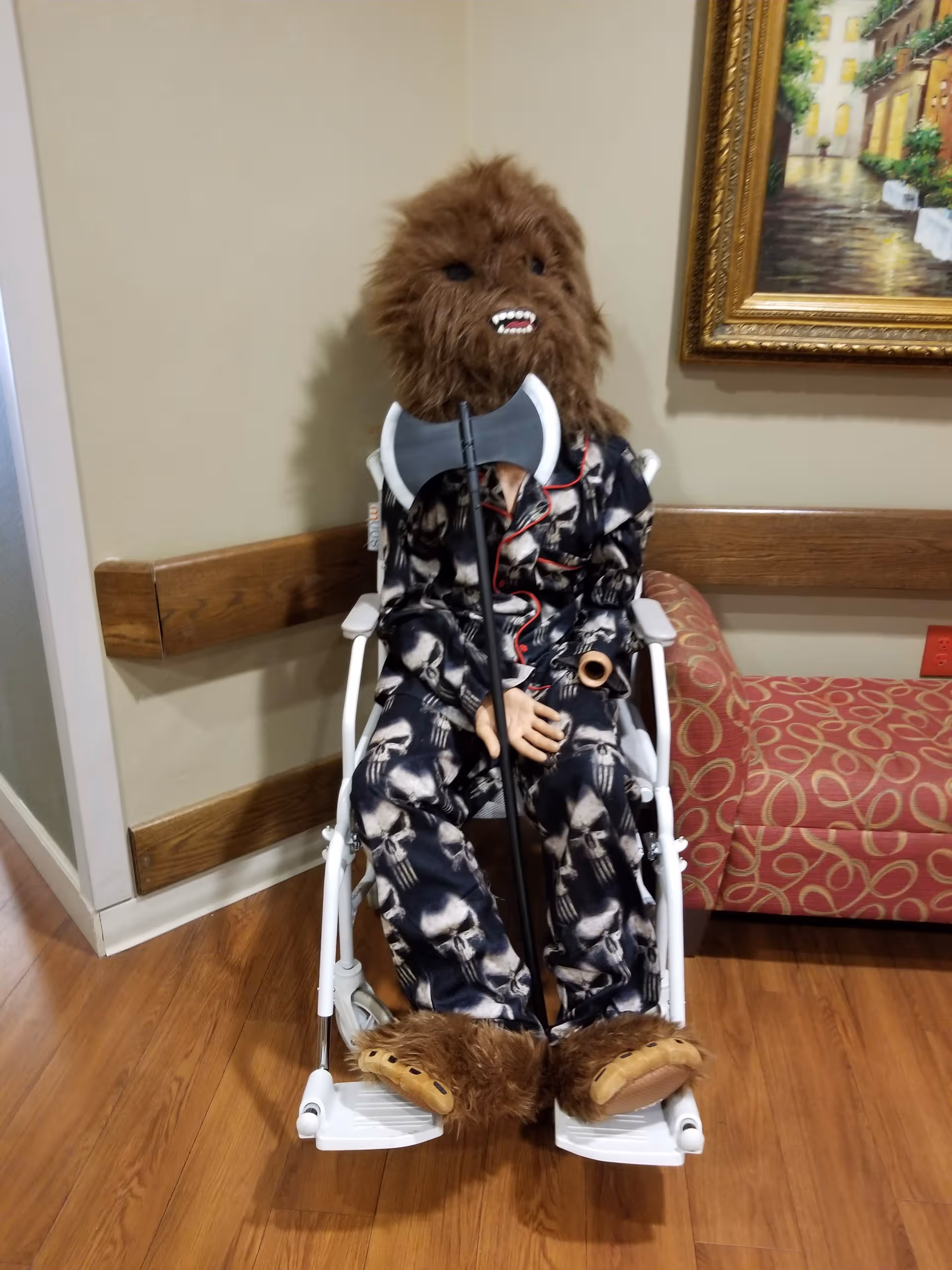Furry Chewbacca-like figure in a wheelchair sits in a hallway.