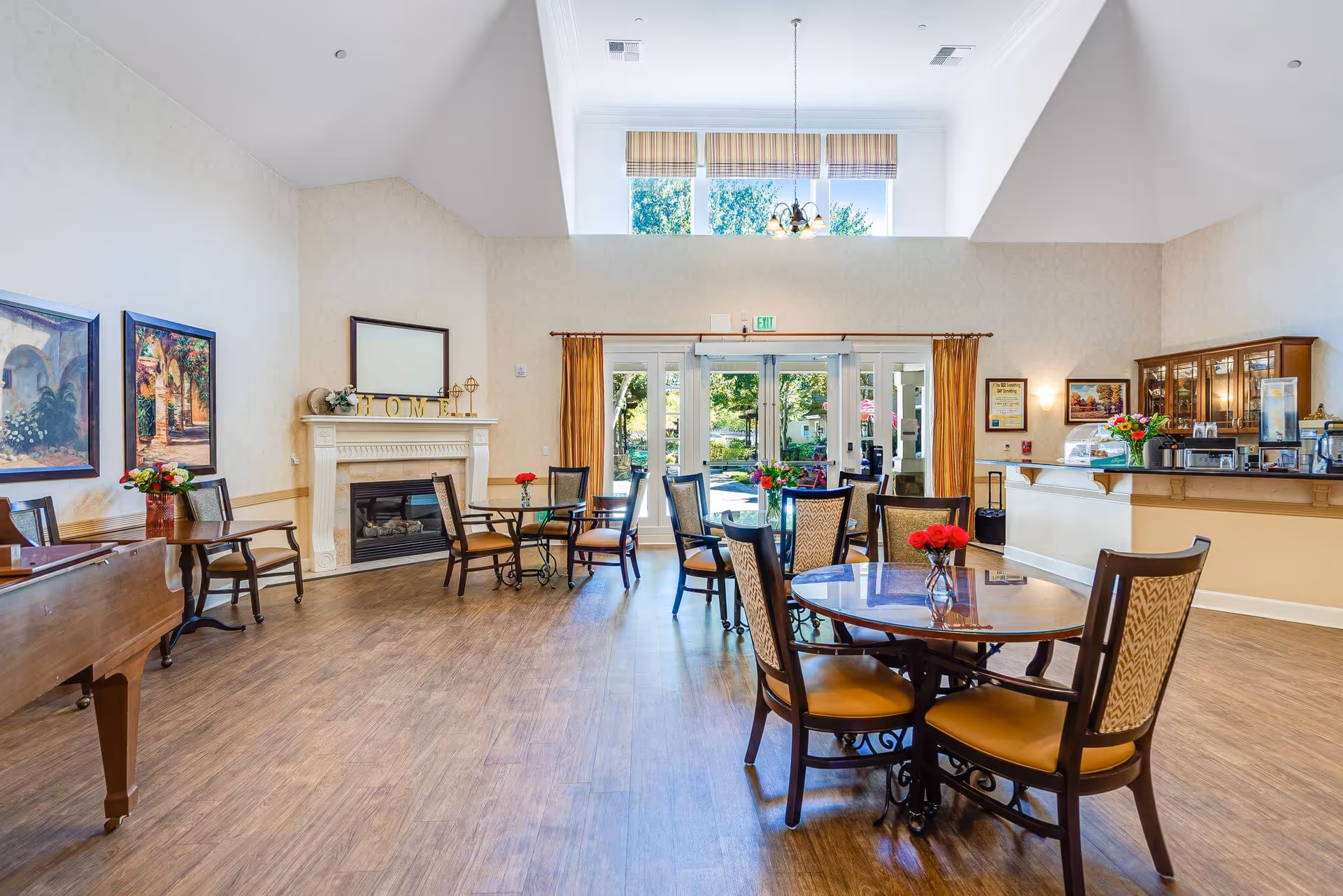 Bright senior living dining area with round tables, chairs, and a fireplace.