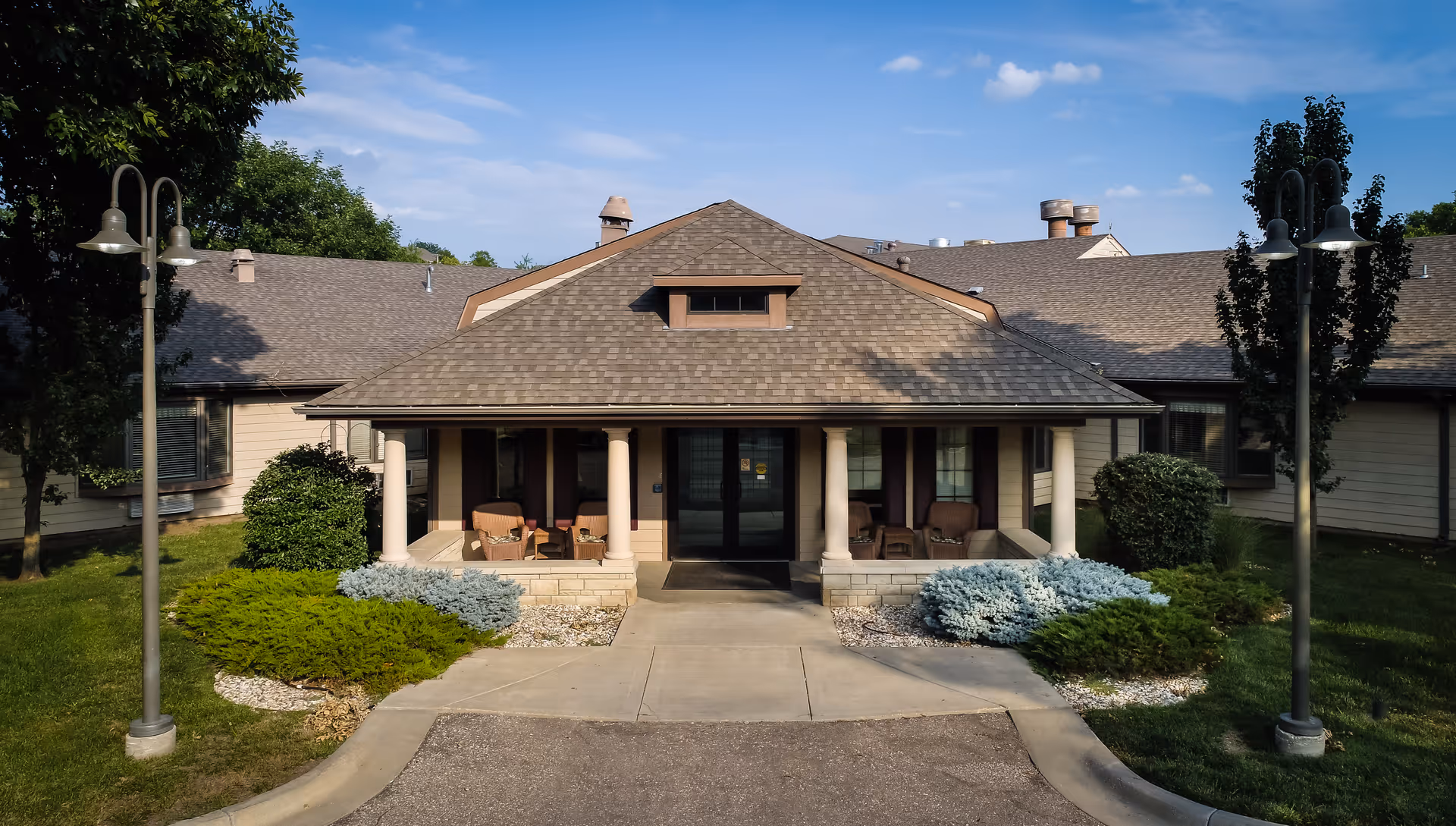 Single-story senior living facility front entrance with columns, seating, and manicured landscaping.