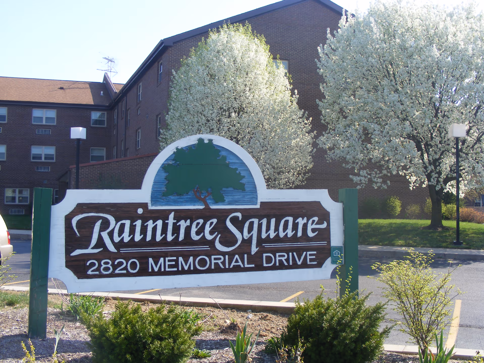 Exterior view of Raintree Square sign in front of a brick building with trees.