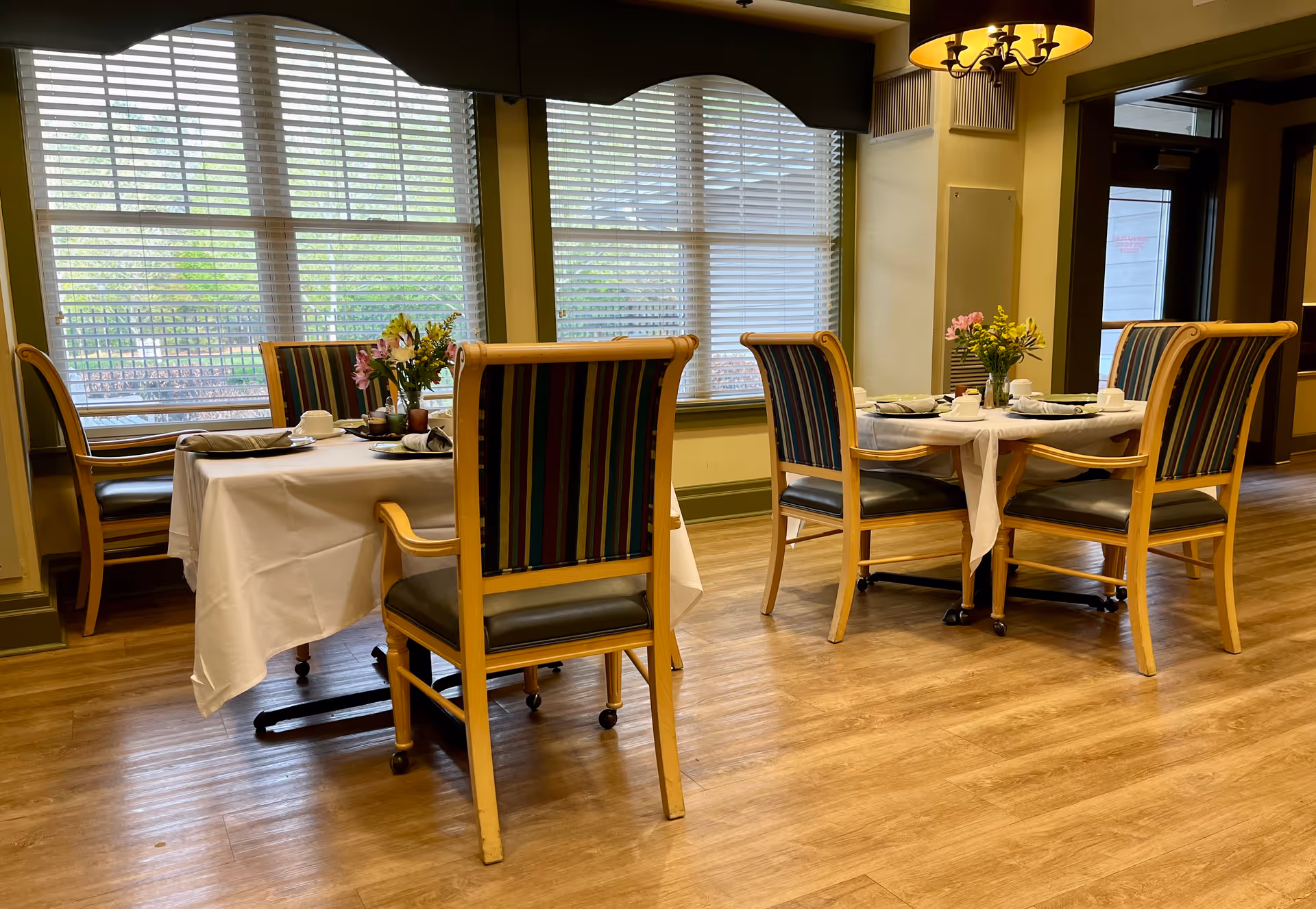 Empty dining room with round tables, white tablecloths, and striped wooden chairs.