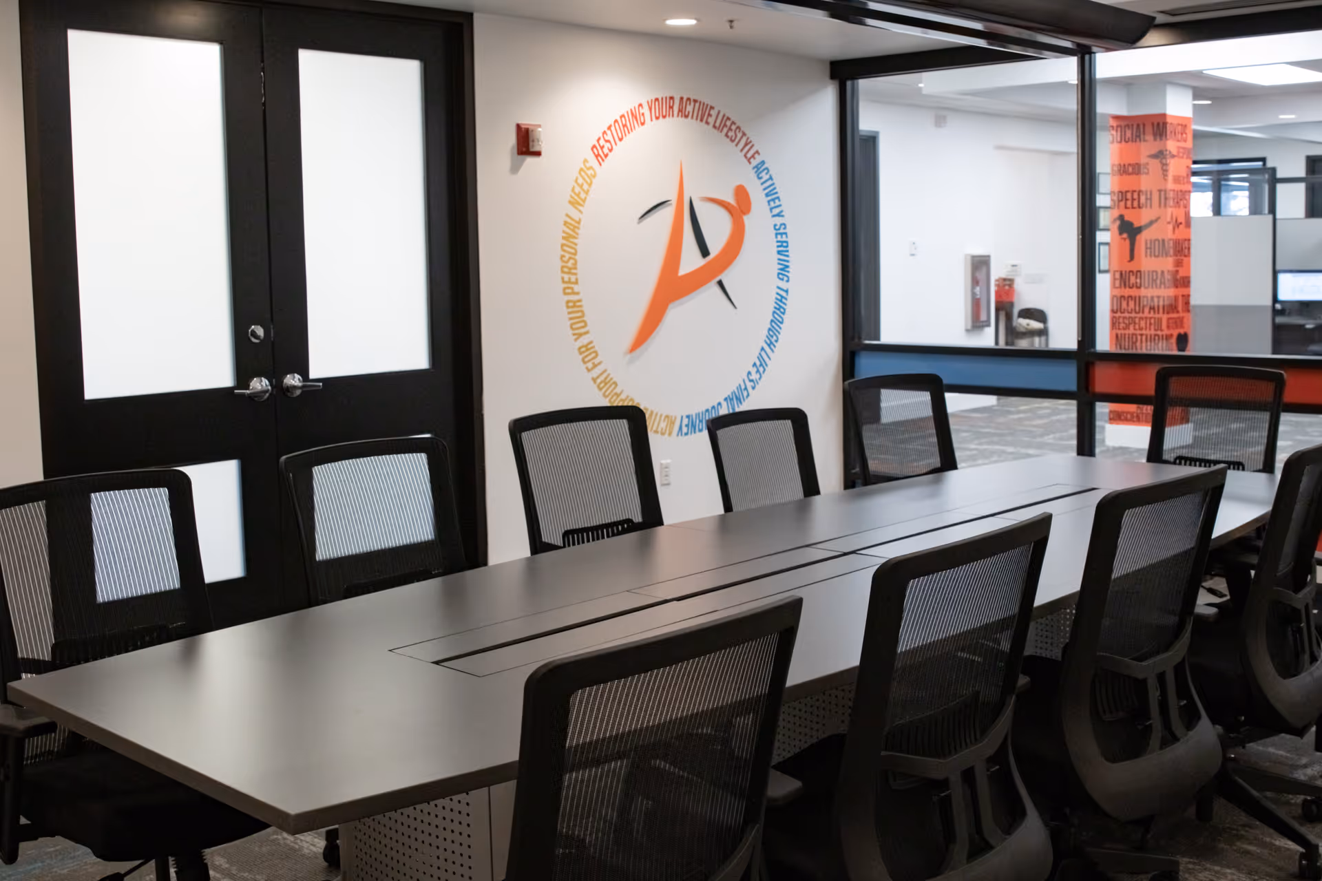 Modern conference room with a long table, mesh chairs, and a circular logo on the wall.