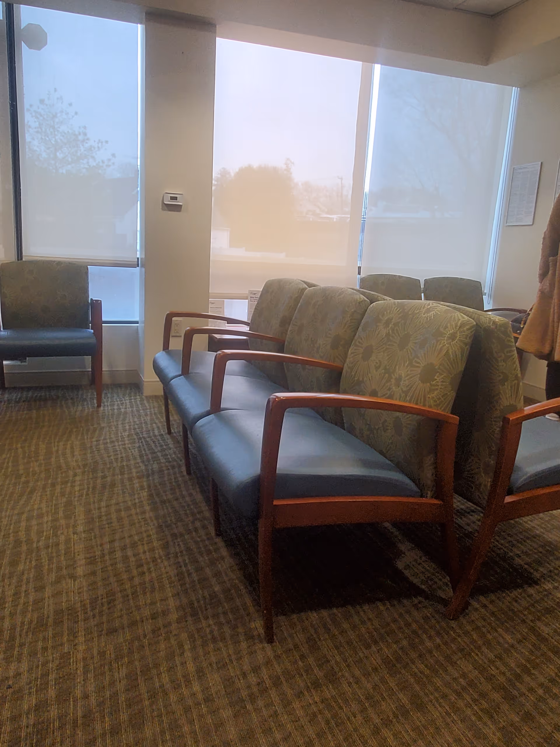 Interior waiting area with blue cushioned chairs and large windows.