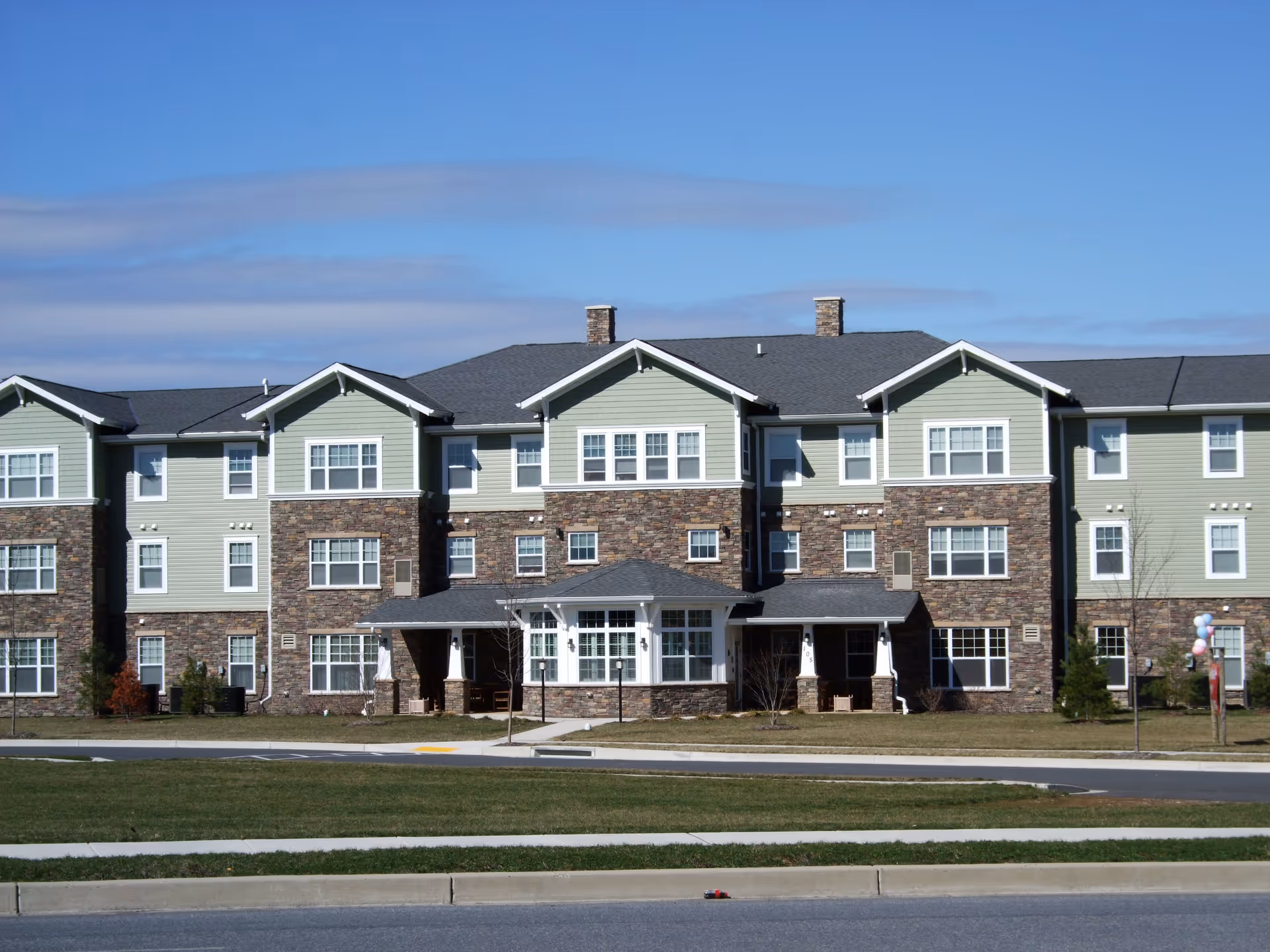 Three-story residential building with stone and light-green siding and a covered central entrance.