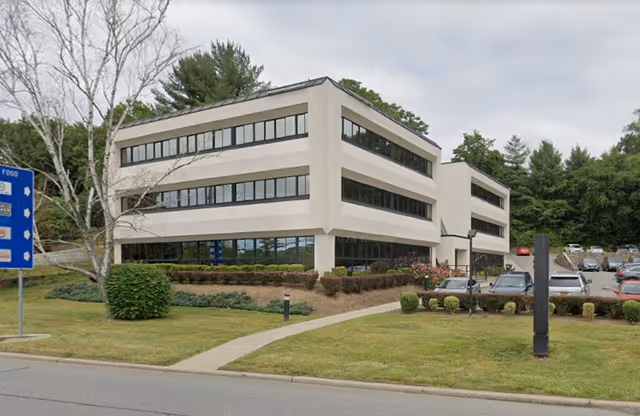 Three-story beige senior living facility exterior with large windows and a parking lot.