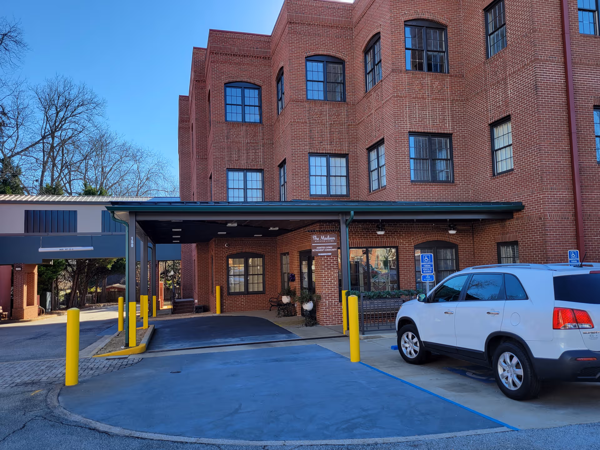 Brick-front assisted living facility entrance with a covered drive-through and a parked SUV.