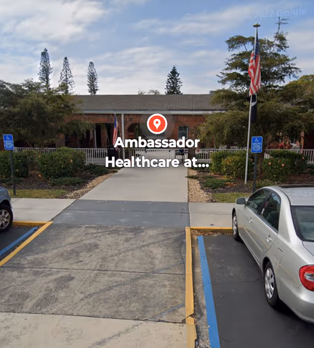 Front exterior of Ambassador Healthcare at College Park with entrance path and parked cars.