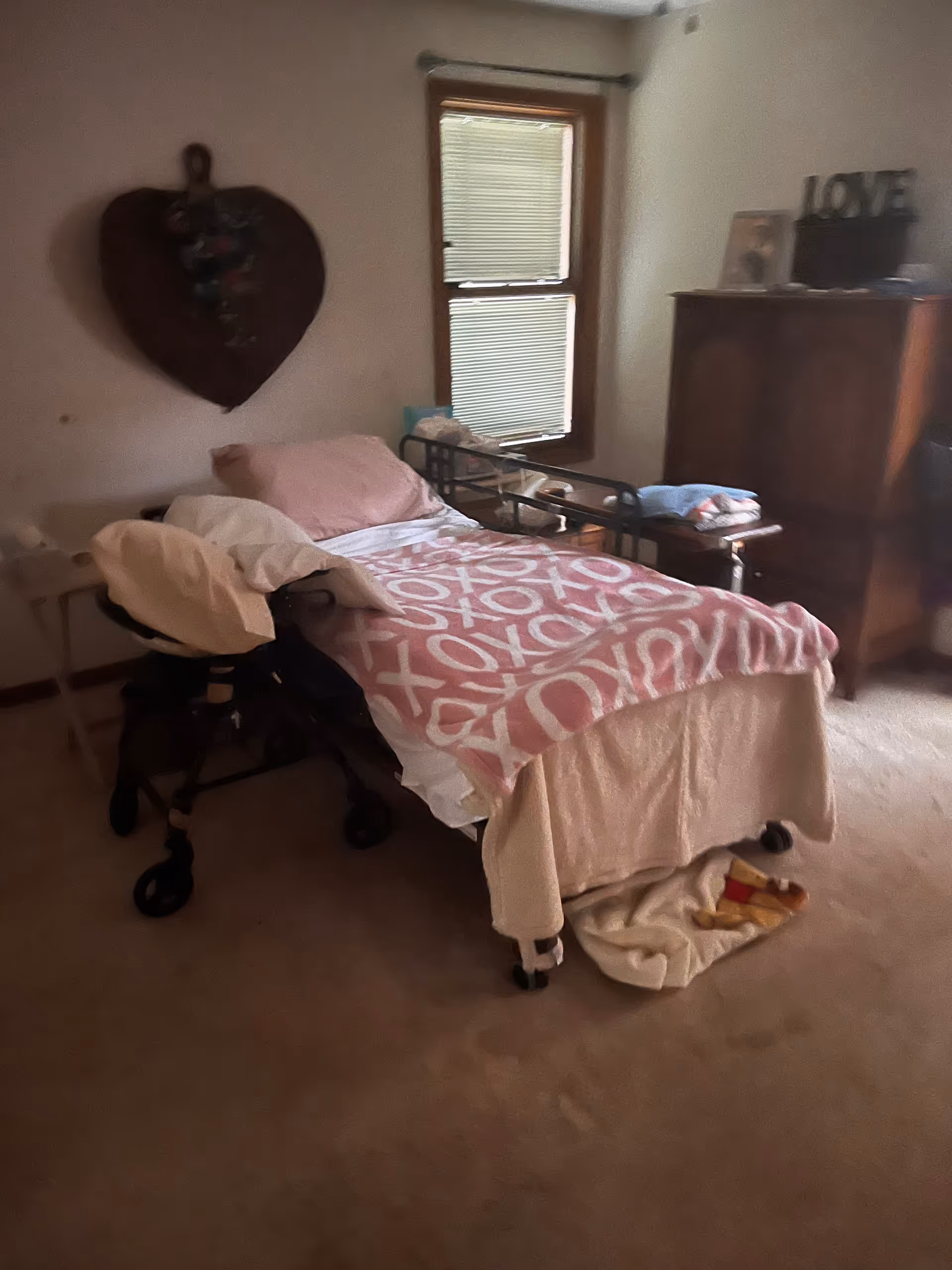A cozy bedroom with a bed, walker, dresser, and decorative heart on the wall.