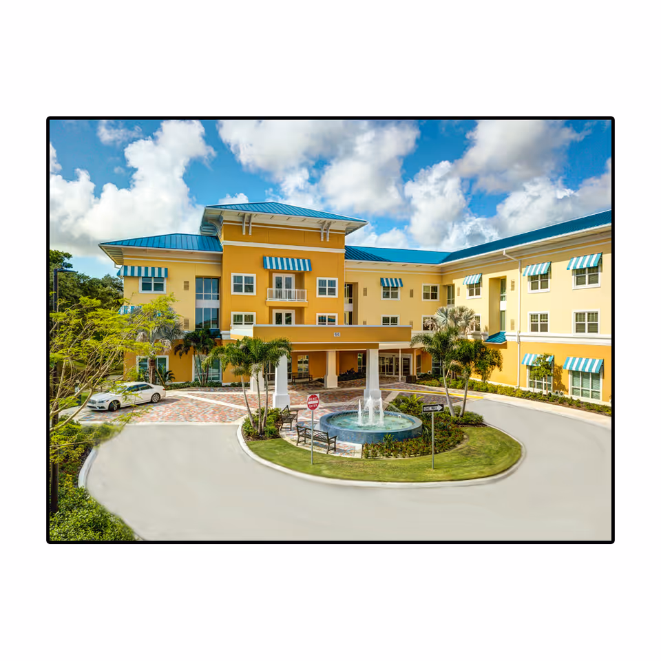 Yellow senior living facility exterior with blue roof and central fountain.