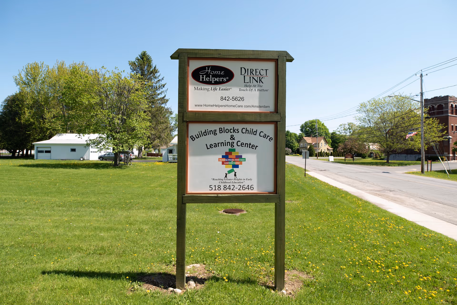 Outdoor wooden signboard on a grassy lot advertising Home Helpers Home Care Amsterdam, NY