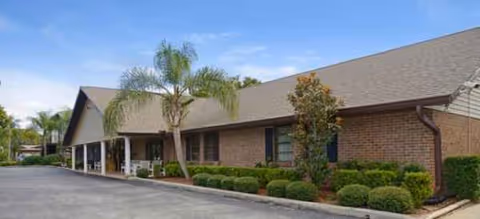 Single-story brick senior living building with palm trees and manicured shrubs.