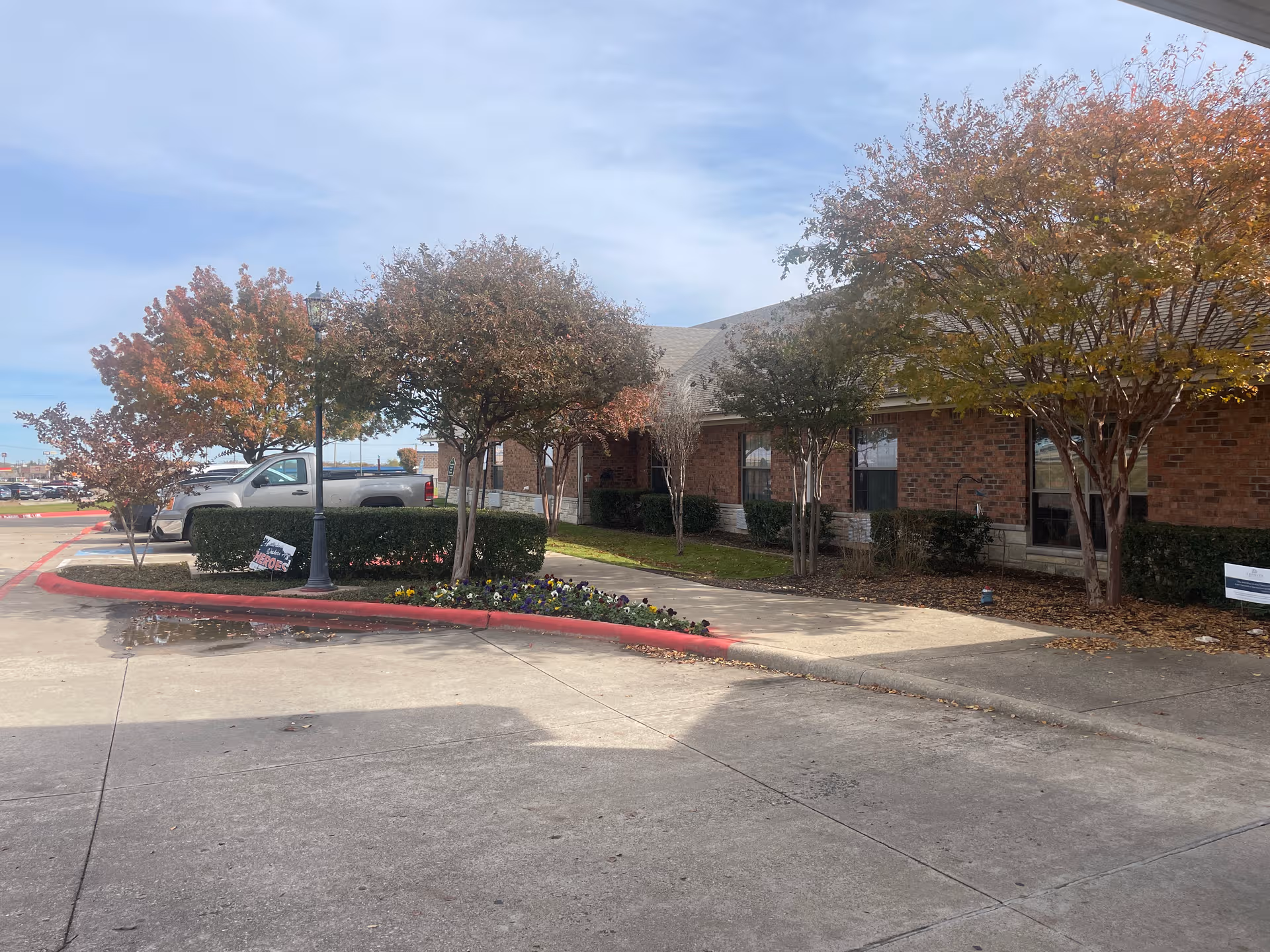 Brick facility exterior with trees, shrubs, and a pickup truck parked out front