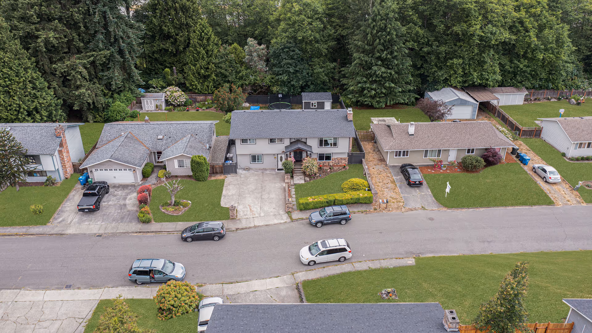 Aerial view of a suburban street with several single-family homes and parked cars.