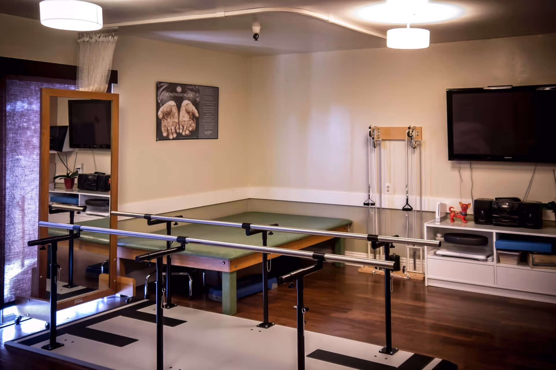 Rehabilitation studio with parallel bars, mat, and a mounted TV inside a quiet room.