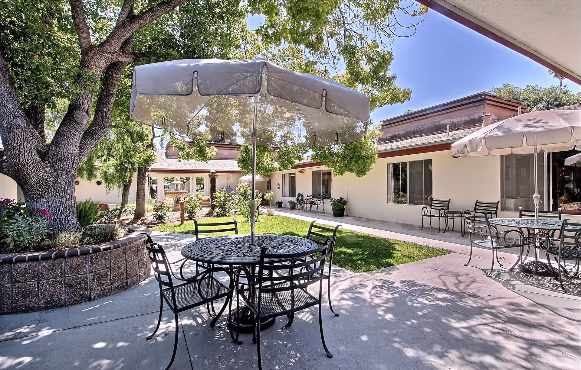Outdoor courtyard of The Vineyards Healthcare Center with metal furniture, umbrellas, and shade trees.