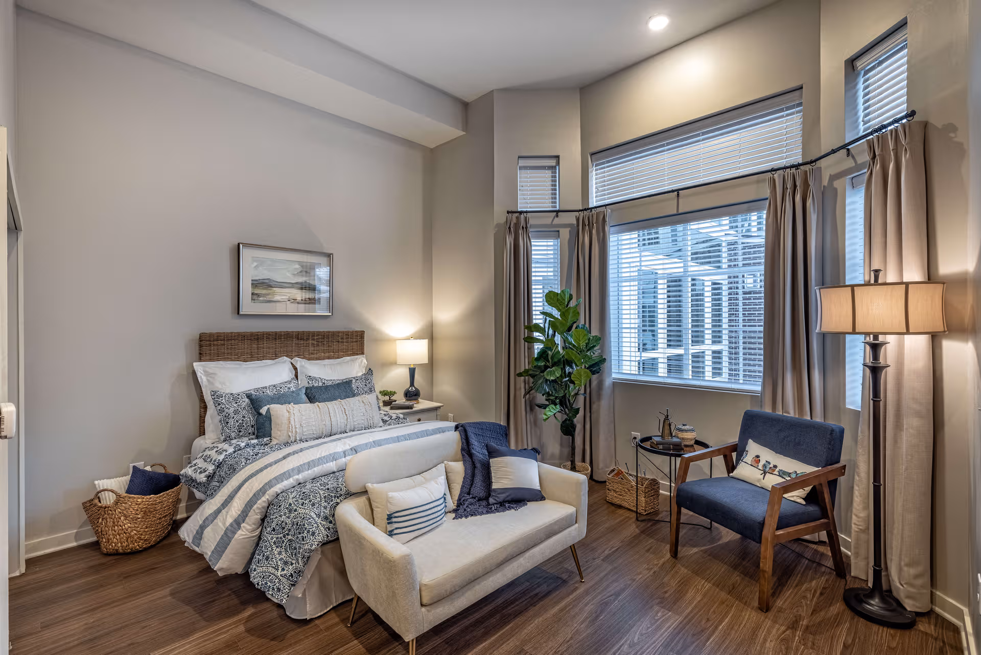 A modern bedroom with a queen bed, seating area, and large windows.